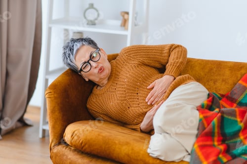 Preview: Senior woman experiencing stomach pain discomfort on couch