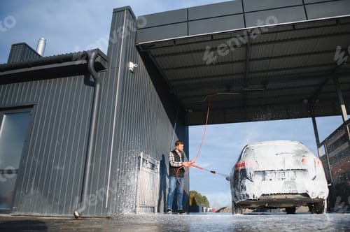 Preview: Car wash equipment. A man is washing a car at self service car wash. High pressure vehicle washer ma