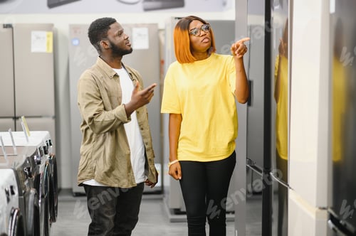 Preview: Young couple, satisfied customers choosing fridges in appliances store