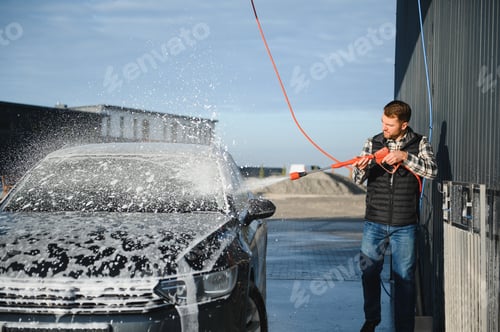 Preview: A man washes off the foam while washing the car. A vehicle is engulfed in soapy foam during a car wa