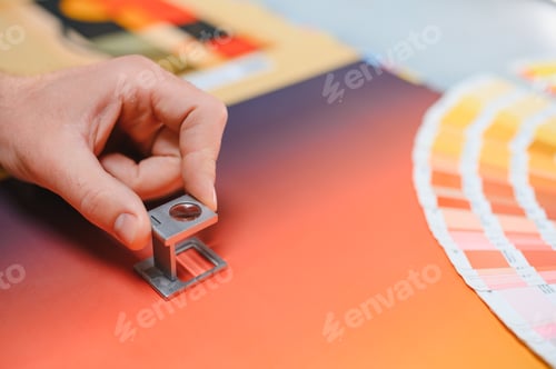 Preview: Hand holding loupe inspecting color swatches in printing house