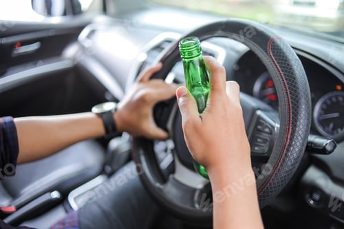 Preview: Close up of Person Holding an Open Green Glass Bottle While Driving Implying Dangerous Drunk Driving
