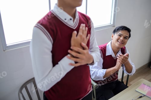 Preview: Student Proudly in Uniform While Classmate Claps and Smiles in Background Classroom Setting