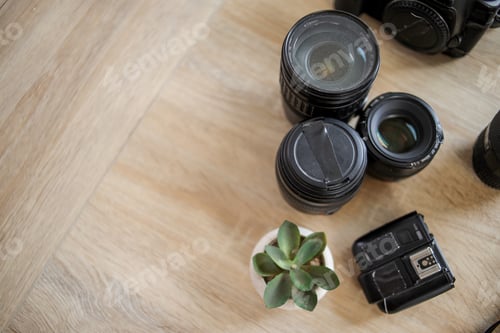 Preview: Top View of Professional Camera Lenses, Flash Trigger, and Small Plant on Light Wooden