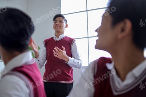 Preview: Young Male Student Stands by Bright Window, Gesturing with His Hands While Speaking to His Peers