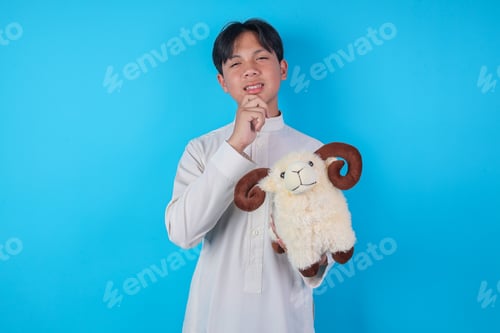 Preview: Thinking Asian Muslim Boy Holding Sheep Doll In Chin Gesture For Eid Al Adha