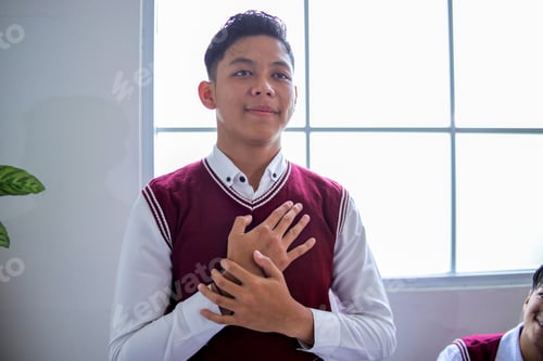 Preview: Closeup of Proud Asian High School Student Standing with His Hands Over His Heart in Class