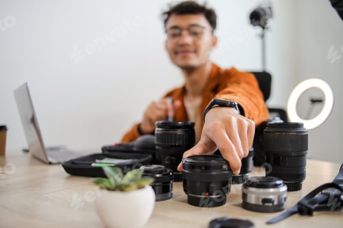 Preview: Close up of Photographers Hand Reaching for One of Several Professional Camera Lenses on Studio Desk