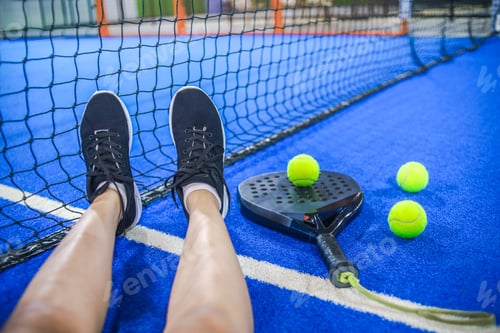 Preview: Point of View of Player Resting Legs Against Net on Blue Padel Court