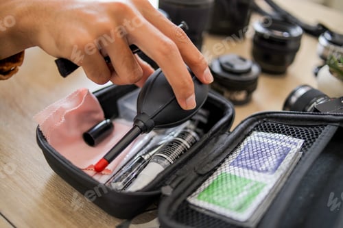 Preview: Close up Hand Picking up Rubber Air Blower From Camera Cleaning Kit Bag on Wooden Table with Lenses