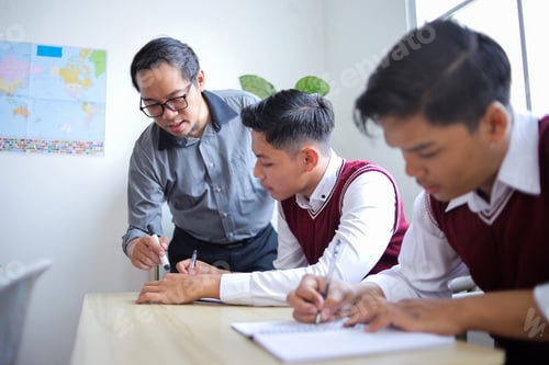 Preview: Male Asian Teacher with Glasses Guiding High School Students Writing in Notebooks