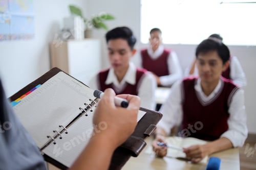 Preview: Closeup of Teacher Hand Holding Notebook and Marker Pen with High School Students in Uniform Sitting