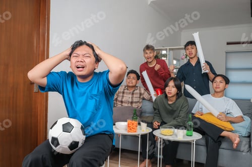 Preview: Anxious Indonesian Football fan Holding His Head While Watching Match with Friends at Home