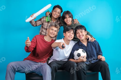 Preview: Cheerful Indonesian Men Enjoying Watching Football, Smiling and Pointing Remote Control at Screen
