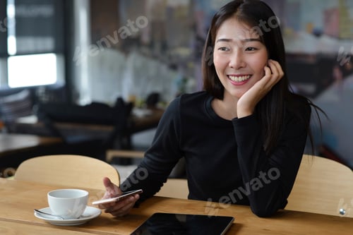 Preview: Happy Asian woman smiling while holding smartphone during professional online remote business work i