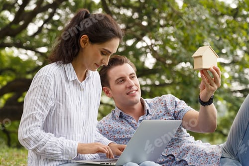 Preview: Happy young man and woman caucasian couple sitting in green park planning their future. Woman using