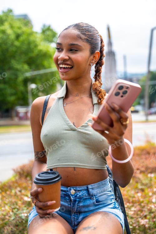 Preview: Young woman smiling using smartphone drinking coffee outdoors