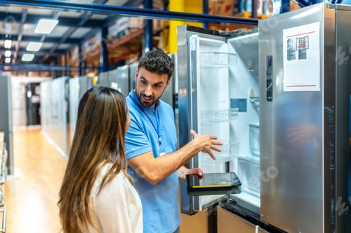 Preview: Salesman explaining refrigerator features to woman in appliance store