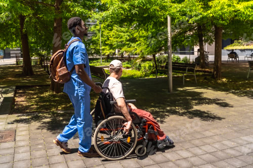 Preview: Male nurse pushing disabled man in wheelchair in park