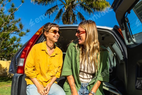 Preview: Happy women laughing sitting in car trunk on road trip