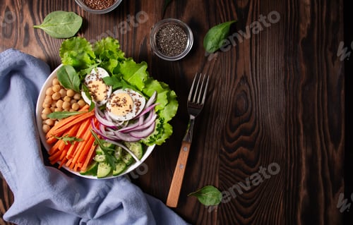 Preview: Balanced salad with green lettuce, cucumber, boiled eggs and chickpeas for lunch on wooden table. To