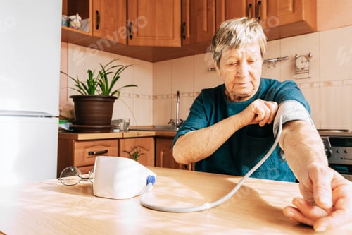 Preview: An elderly woman measures her blood pressure in the kitchen. Health maintenance, healthy aging, dise
