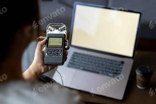 Preview: Person Holding Audio Recorder Near Laptop with Blank Screen