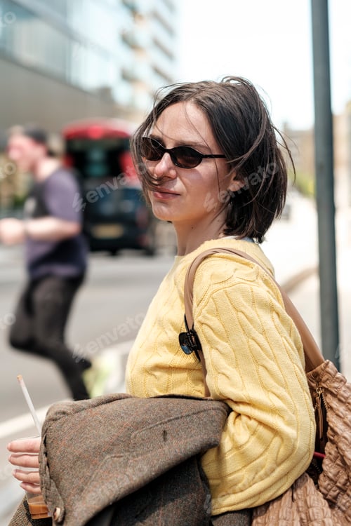 Preview: Woman wearing sunglasses enjoying iced coffee in urban street