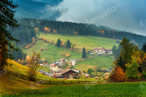 Preview: Alpine Santa Maddalena village on lush green hill during autumn and morning mist in Dolomites, Italy