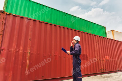 Preview: Male logistics engineer uses walkie talkie while walking and inspecting stacked shipping containers
