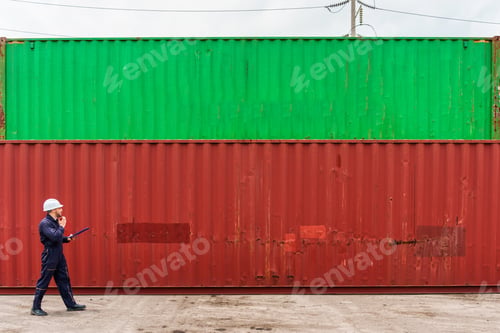 Preview: Male logistics engineer uses walkie talkie while walking and inspecting stacked shipping containers