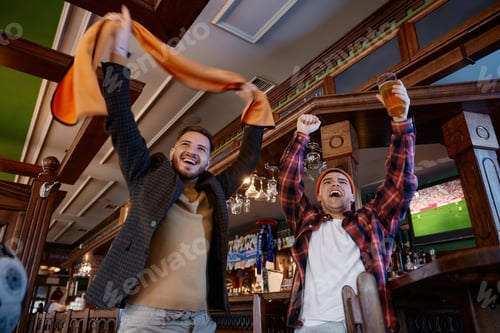 Preview: Men celebrating football game loudly. Joyful men with raised scarves. Two men cheer in pub