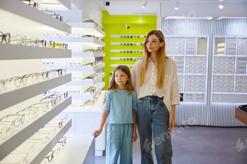 Preview: Mother and child explore fashionable spectacles together in well-lit optical retail environment