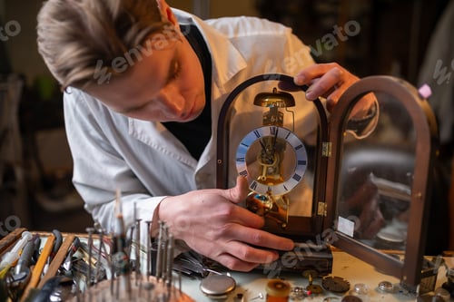 Preview: Watchmaker repairing vintage mechanical mantel clock in workshop