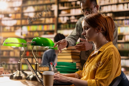 Preview: Student and mentor discuss ideas beside laptop in library study area desk