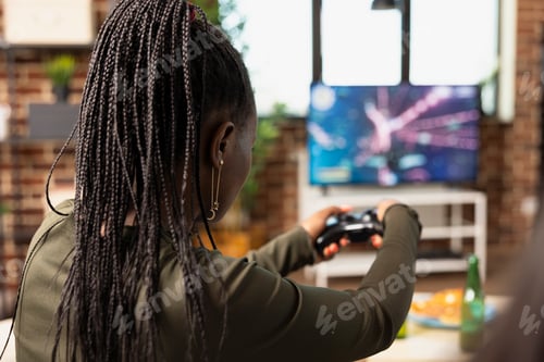 Preview: Young black woman playing console game on couch