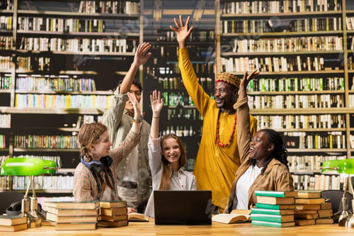 Preview: Students raising hands after high five gesture and smiling in library