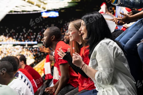 Preview: Excited female soccer fans leaning forward and cheering from stadium seats