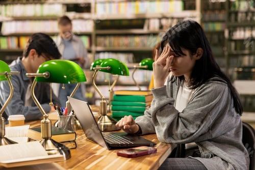 Preview: Stressed university student with headache in library during exam preparation