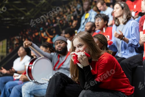Preview: Young female football supporter holding red scarf to mouth