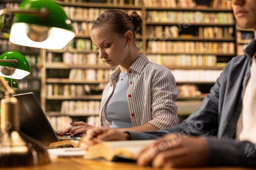 Preview: Focused student typing on laptop beside open book at library table