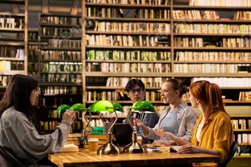 Preview: University students talk through coursework at library table with open books