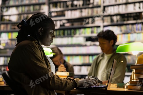 Preview: African american student with braided hair typing on laptop at library table
