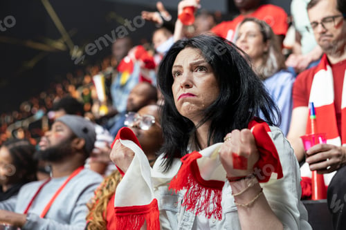 Preview: Upset mature female football supporter clutching red and white scarf in stands