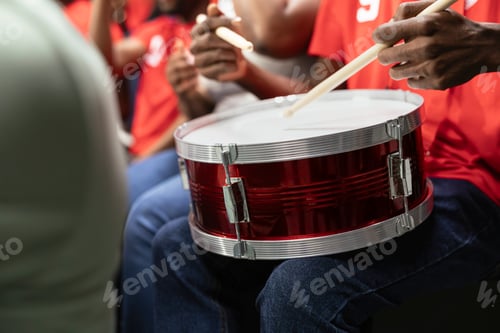 Preview: Close-up of red supporter drum on football fan lap during stadium chant