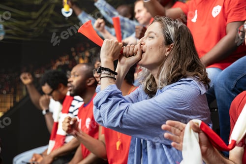 Preview: Passionate woman football fan blowing red vuvuzela in stadium stands