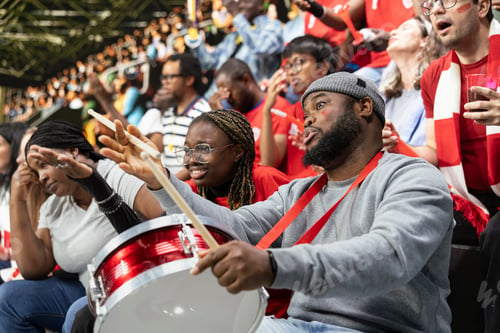 Preview: Red team football supporter with drum reacting in crowded stadium stands