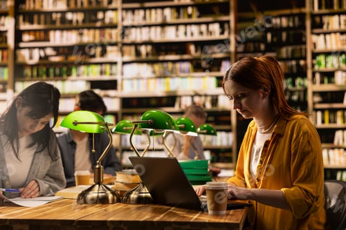 Preview: Student working on laptop at library desk with coffee nearby at wooden table