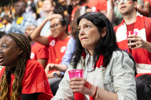 Preview: Worried mature female football supporter holding pink cup and red scarf
