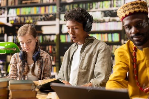 Preview: Student wearing headphones reading open book at library table